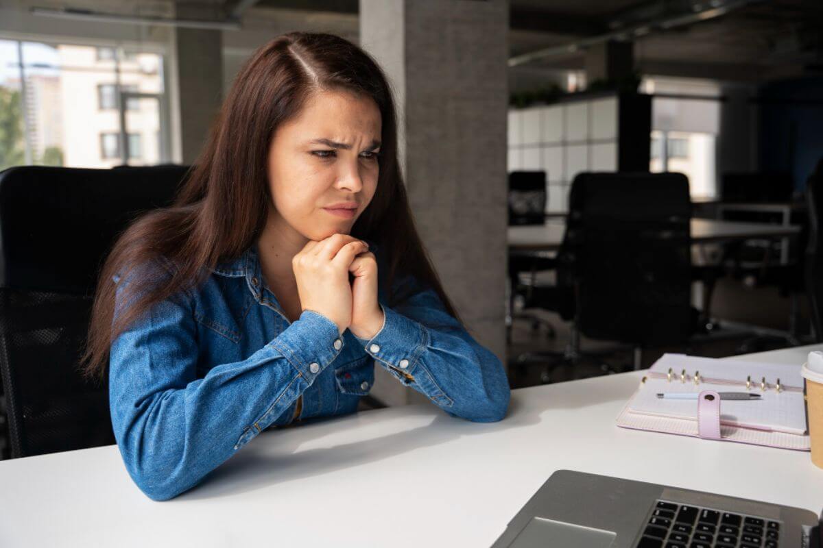 Young woman in an office pausing during a discussion, showing hesitation and concern about expressing ideas clearly in a professional setting.