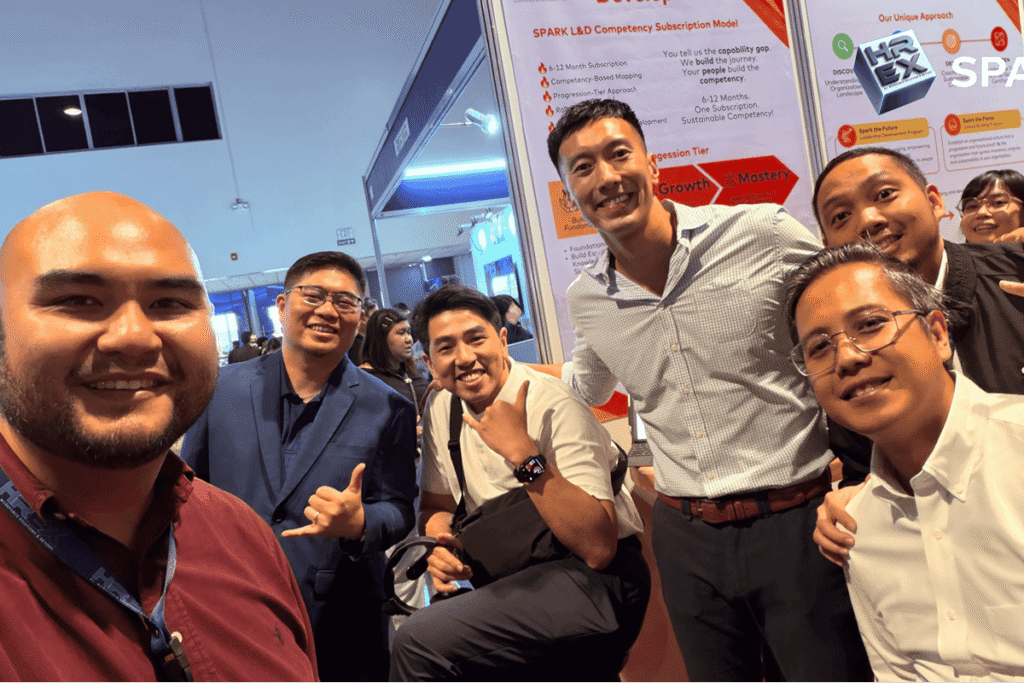 Colleagues posing for a selfie portrait near the SPARK competency subscription model display.