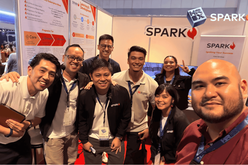Team members celebrating and smiling together during the exhibition event in front of the main SPARK banner.