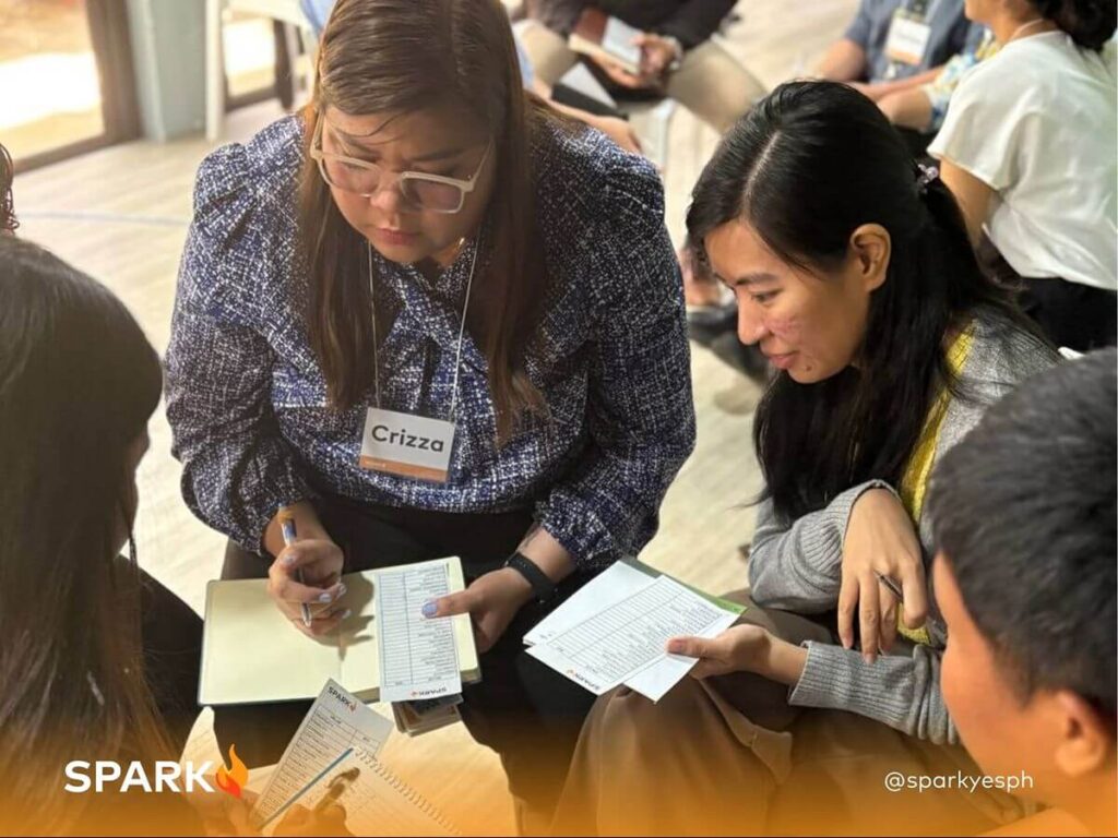 Spark PH team-building participants working together on a group activity involving worksheets and discussion to strengthen communication and collaboration