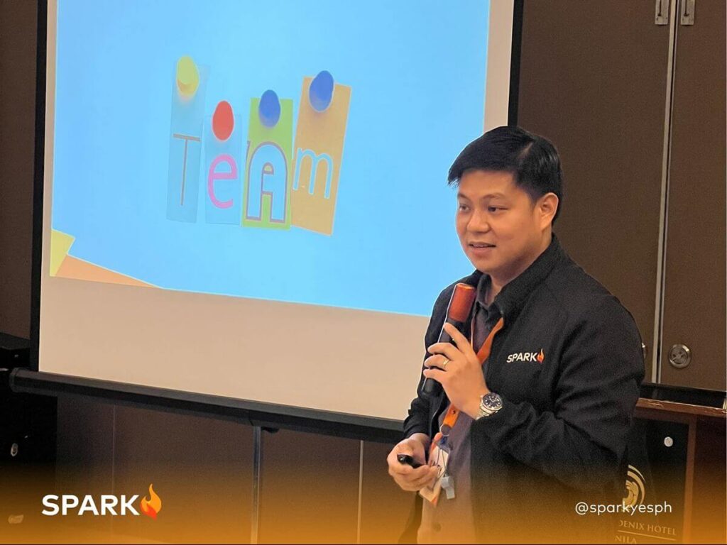 Spark PH facilitator speaking into a microphone during a team-building workshop focused on workplace inclusivity and collaboration